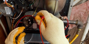 A technician wearing gloves uses a multimeter to test wiring inside a furnace for BV Air Conditioning & Heating in Dallas, TX.
