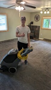A happy technician giving a thumbs up next to a carpet cleaning machine after a job by Alaska Floor Care Specialists in Fairbanks, AK.