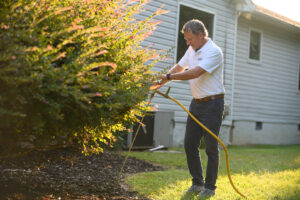 A pest control technician applying treatment to bushes around a home for Lookout Pest Birmingham, AL.