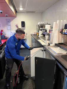 A technician from Ideal Pest Control Inc treating a cabinet in a commercial kitchen in Miami, FL.