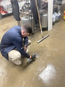A pest control technician applying treatment to a floor drain in a commercial kitchen at Devlins Pest Control in Reading, PA.