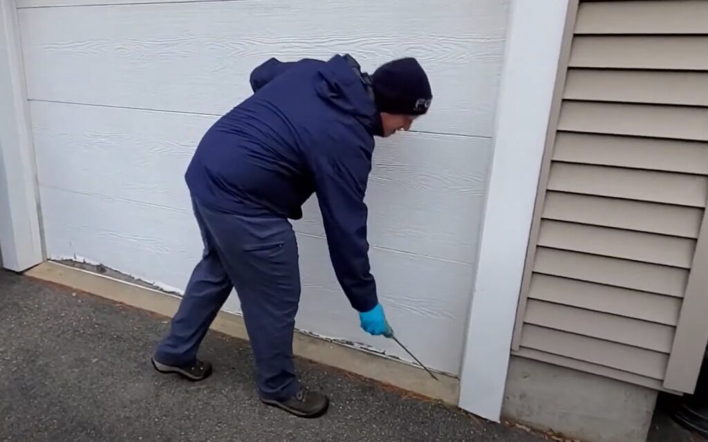 A pest control technician treating the garage door area for pests at a residence for Richmond Pest Control in Richmond, KY.