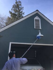 A Longeway Pest Control technician treating a garage light fixture and eave with a long pole tool in Oakland, CA.