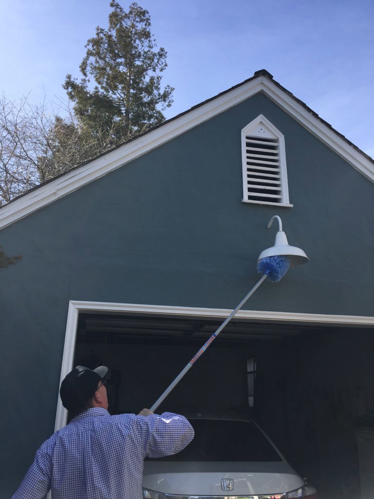 A Longeway Pest Control technician treating a garage light fixture and eave with a long pole tool in Oakland, CA.