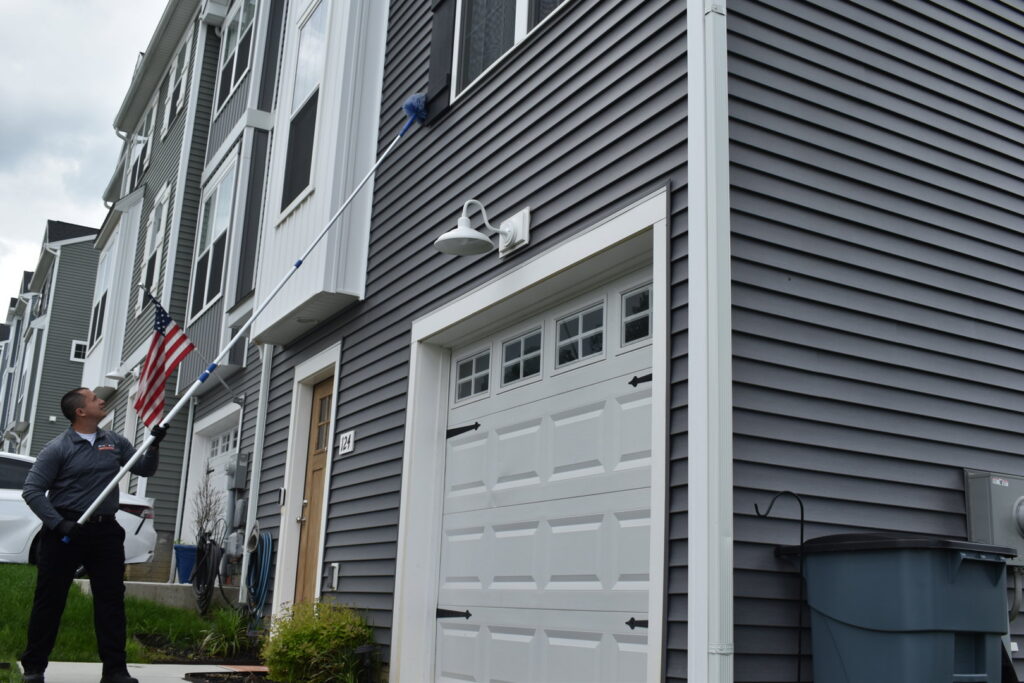 A Bye Bye Pest Solutions technician using a long pole to treat the eaves of a house for pest control in Hanover, PA.
