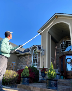A Nature Shield Pest & Lawn technician treating the eaves of a house with a long pole in Meridian, ID.