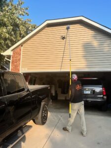 A pest control technician treating the exterior of a house with a long pole for pests by Elite Pest Control in Maple Grove, MN.
