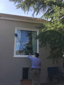 A Longeway Pest Control technician treating around a house window with a long pole tool in Oakland, CA.