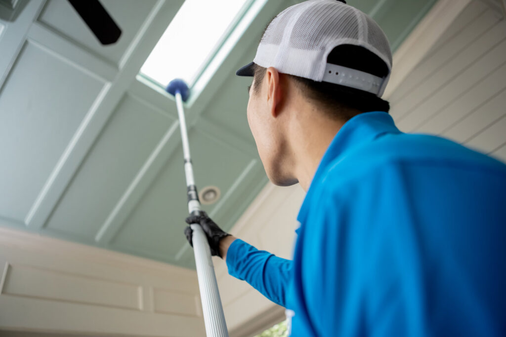 A Pest Authority Des Moines technician treating an interior ceiling or skylight with a long pole tool in Des Moines, IA.