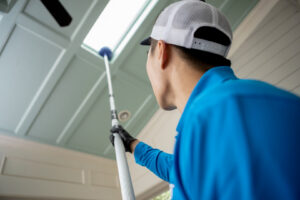 A Pest Authority Des Moines technician treating an interior ceiling or skylight with a long pole tool in Des Moines, IA.