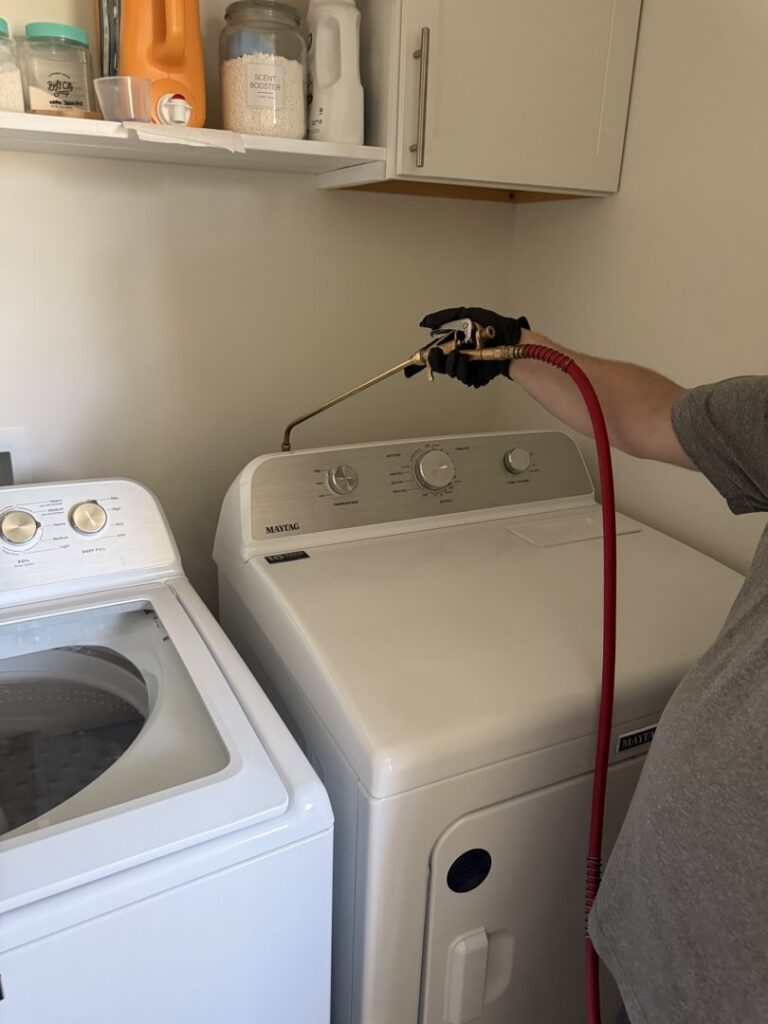 A Rosie's Pest Control technician applying treatment in a laundry room near appliances in Memphis, TN.