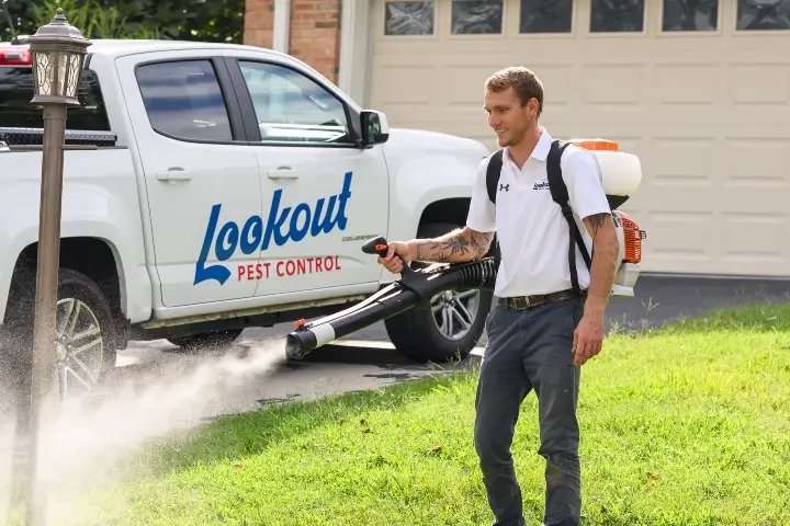 A pest control technician treating a lawn with a backpack sprayer for Lookout Pest Birmingham, AL.
