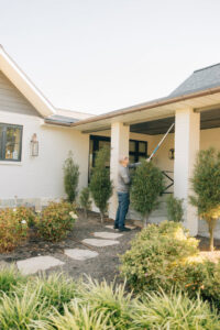 A technician using a long pole to treat high areas on a house porch for Thrive Pest Management in Sandy, UT