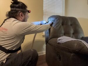 A pest control technician with a headlamp and gloves treating a recliner chair for pests, provided by Tailor Made Pest and Wildlife in Louisville, KY.