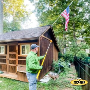 A Noosa Pest Management, LLC technician treating the exterior of a shed with a long pole in Columbia, SC.
