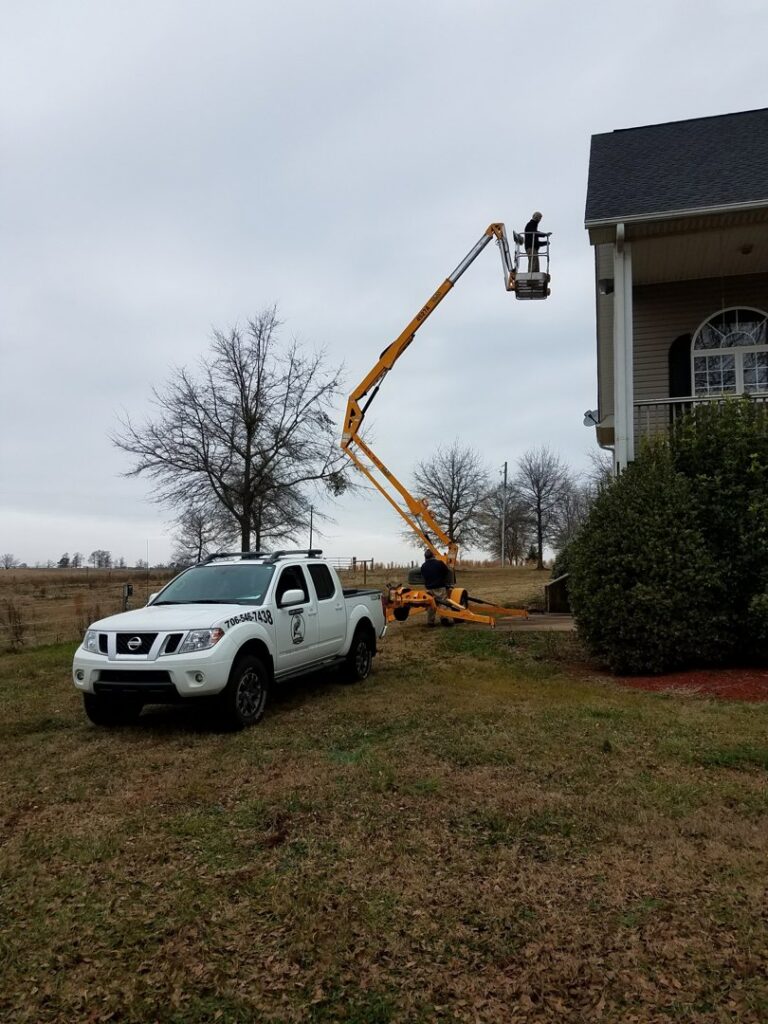 A technician using a boom lift to access a high area of a house for pest control services by Athens Exterminating Inc. in Athens, GA