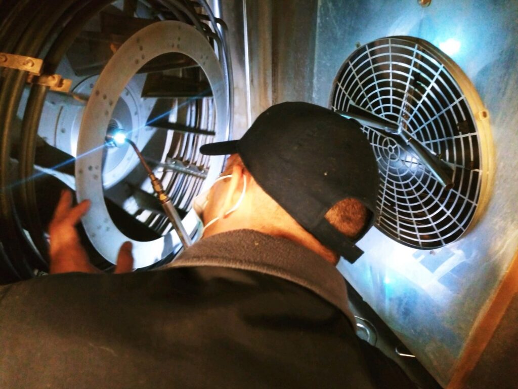 A technician from TJ Mechanical Services LLC welding or brazing inside a large HVAC component in Rock Hill, SC.