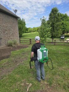 A pest control technician from Titan Pest Pro - Springfield walking with a backpack sprayer in a grassy yard in Springfield, MO.