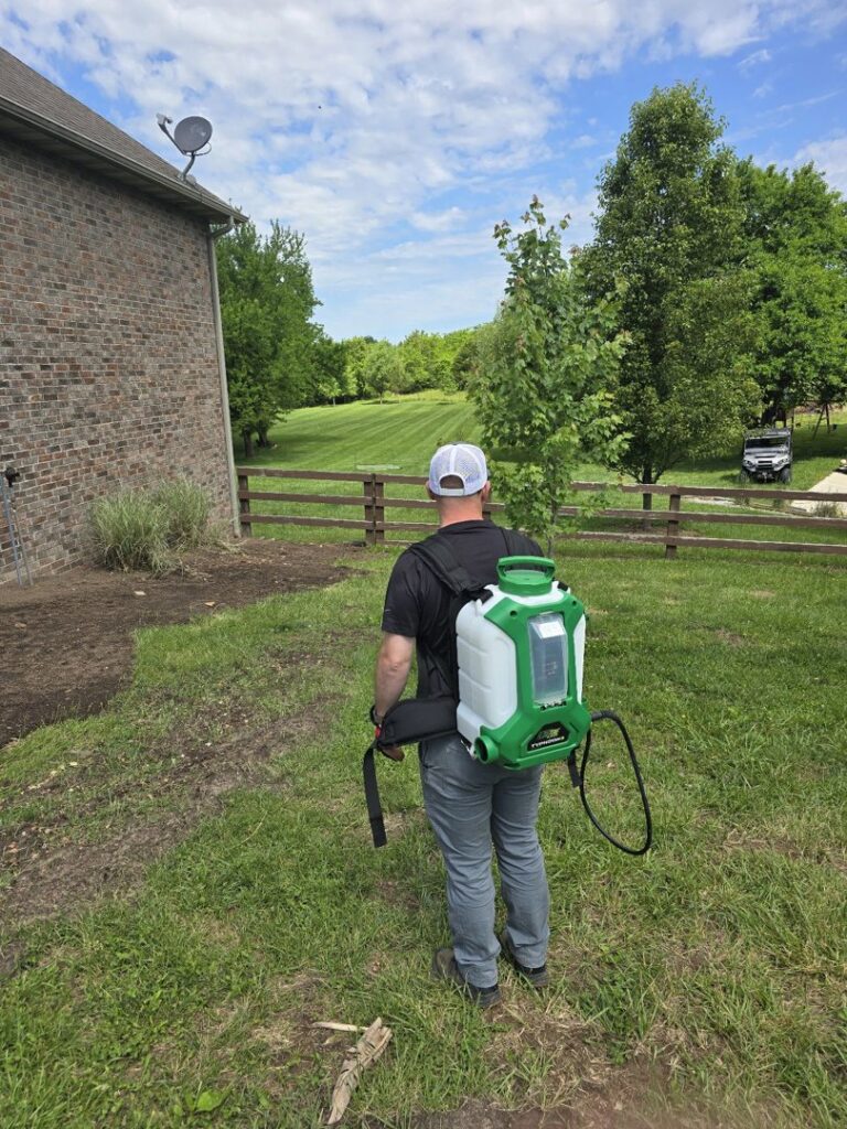 A pest control technician from Titan Pest Pro - Springfield walking with a backpack sprayer in a grassy yard in Springfield, MO.