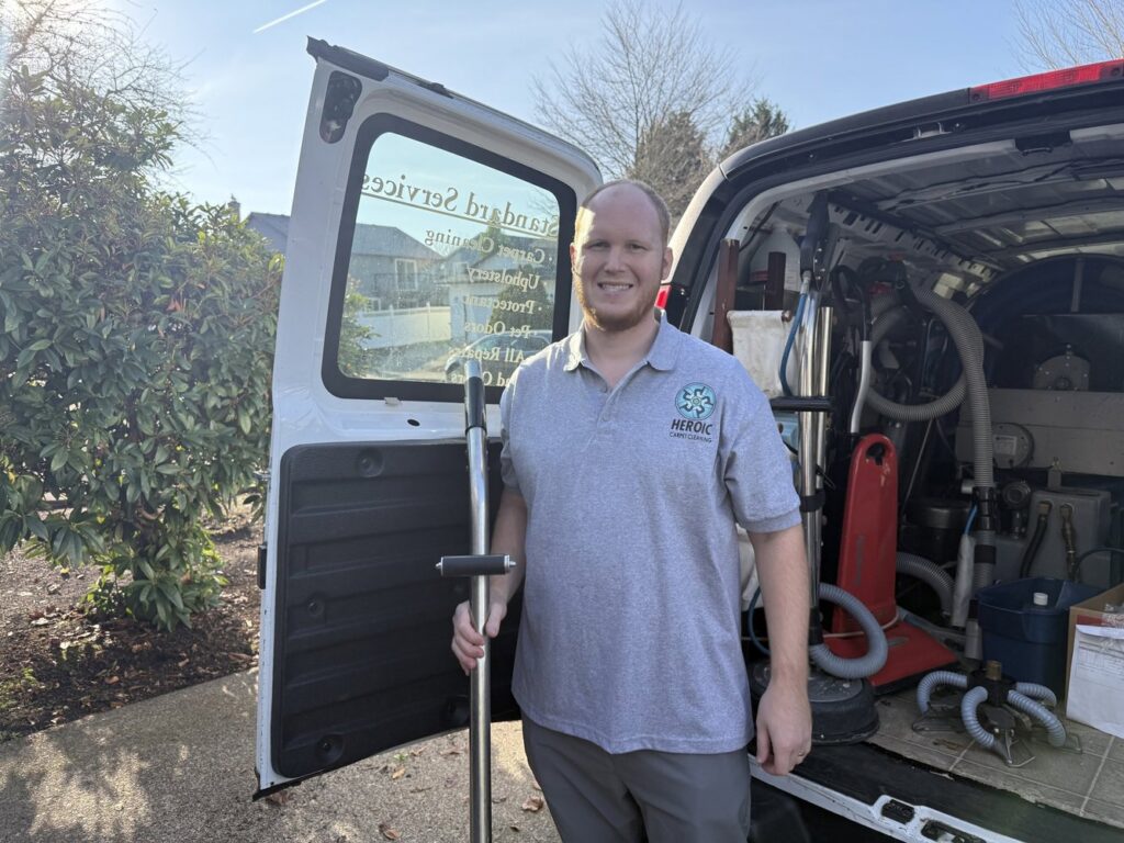 A Heroic Carpet Cleaning Oregon technician holding a cleaning wand, standing by the open service van with equipment in Beaverton, OR