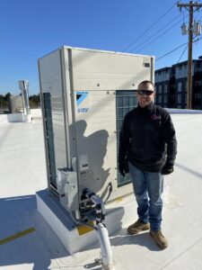 A technician standing next to a Daikin VRV commercial HVAC unit on a rooftop by The Heating Specialist in Portland, OR