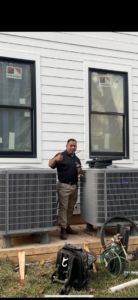 A Vanessa Service HVAC technician giving a thumbs up next to newly installed Carrier AC units in Falls Church, VA.