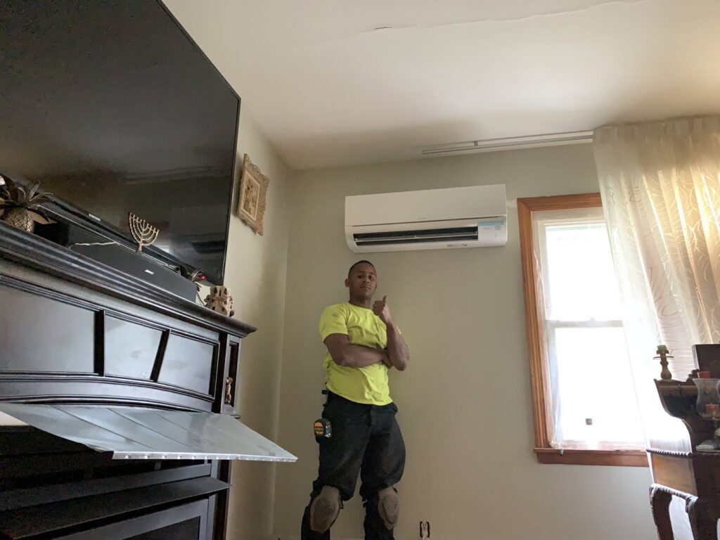 A Hyper Fusion Heating & Cooling technician giving a thumbs up next to a newly installed ductless mini-split indoor unit in Waterbury, CT.