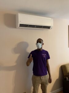 A Hyper Fusion Heating & Cooling technician giving a thumbs up next to a newly installed mini-split indoor unit in Waterbury, CT.