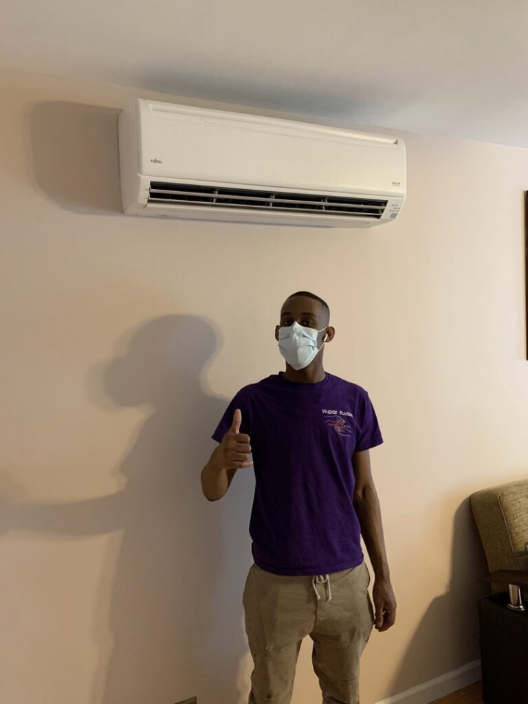 A Hyper Fusion Heating & Cooling technician giving a thumbs up next to a newly installed mini-split indoor unit in Waterbury, CT.