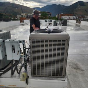 A technician inspecting a newly installed rooftop AC unit by JL Mechanical in Pleasant Grove, UT.