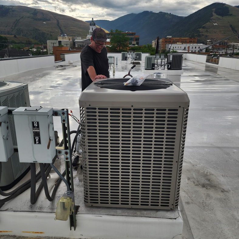 A technician inspecting a newly installed rooftop AC unit by JL Mechanical in Pleasant Grove, UT.