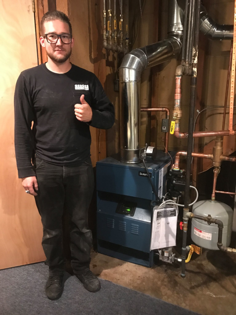 A Geddes Heating and Cooling technician giving a thumbs up next to a newly installed boiler system in Aurora, CO.