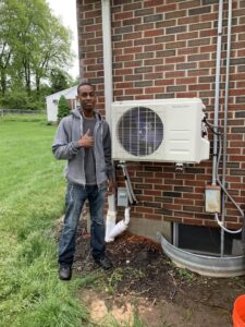 A Hyper Fusion Heating & Cooling technician giving a thumbs up next to an outdoor mini-split condenser unit in Waterbury, CT.