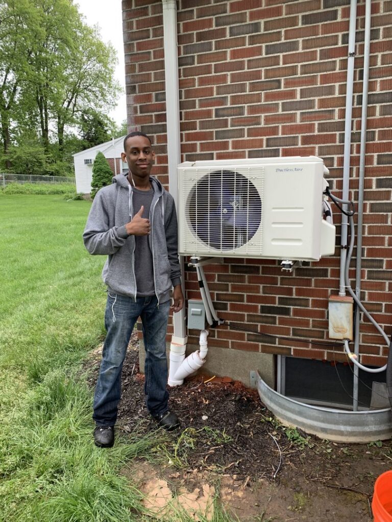 A Hyper Fusion Heating & Cooling technician giving a thumbs up next to an outdoor mini-split condenser unit in Waterbury, CT.