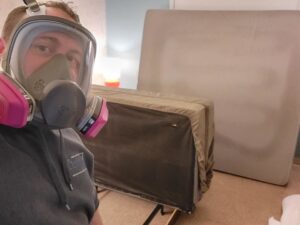A pest control technician wearing a respirator mask, preparing for an indoor pest treatment, likely bed bugs, for Optimum Pest Pros, LLC. in Canandaigua, NY.