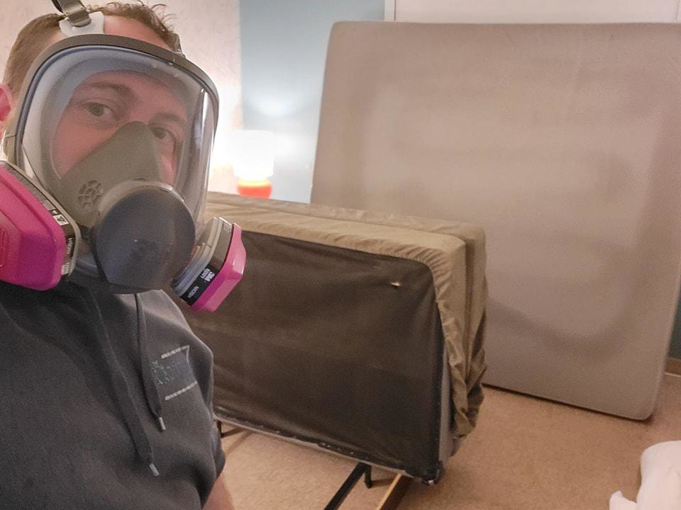 A pest control technician wearing a respirator mask, preparing for an indoor pest treatment, likely bed bugs, for Optimum Pest Pros, LLC. in Canandaigua, NY.