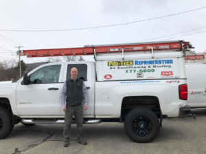 A Pro-Tech Refrigeration technician standing next to a service truck with ladders in Auburn, ME.