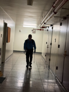 A Pest Lock, Inc. technician with a backpack sprayer walking down a hallway for pest control service in Vancouver, WA.
