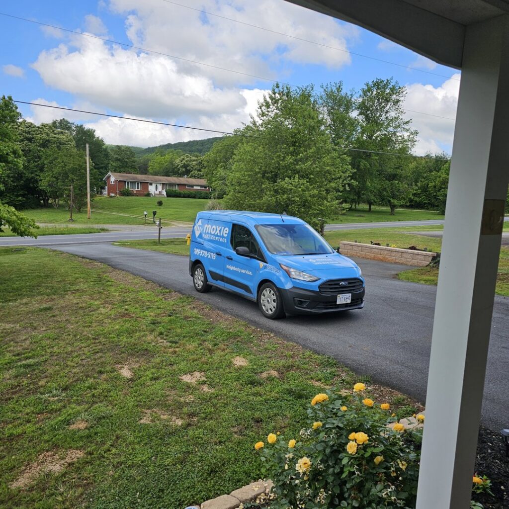 A Moxie Pest Control Charlotte technician holding a sprayer next to a company van in Charlotte, NC.