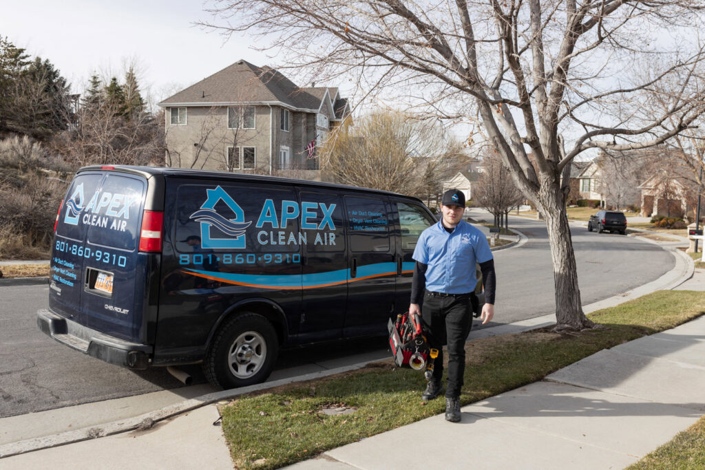An APEX Clean Air technician carrying tools, walking from a service van in South Salt Lake, UT.