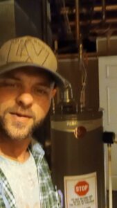 A TAS Mechanical Services technician standing next to a water heater, likely during an installation or service in Kearney, MO.