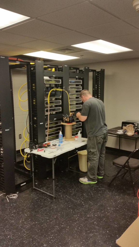 A technician working on fiber optic cabling and network equipment for ECOMM LLC in Atlanta, GA.