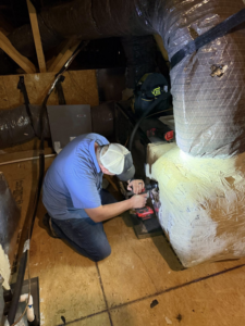 A technician working on an HVAC unit in an attic for All American Heating and Air in Warner Robins, GA.