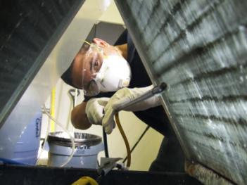 A technician in protective gear working inside an HVAC duct for Ductz of Southeast Michigan in Livonia, MI.