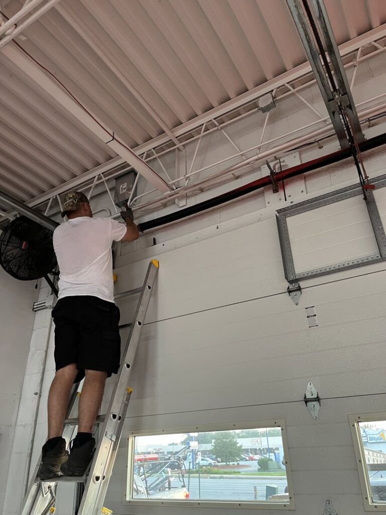 A technician on a ladder working on a commercial garage door system for The Region's Garage Door Repair in Hammond, IN.