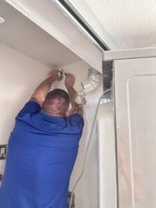 A Duct Dudes technician working on connecting dryer vent ducts behind a washing machine in Scottsdale, AZ.