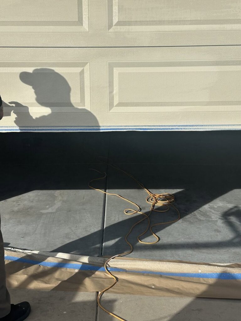 Shadow of a technician working on a garage door, possibly painting or sealing, by Sonoran Garage Doors in Mesa, AZ