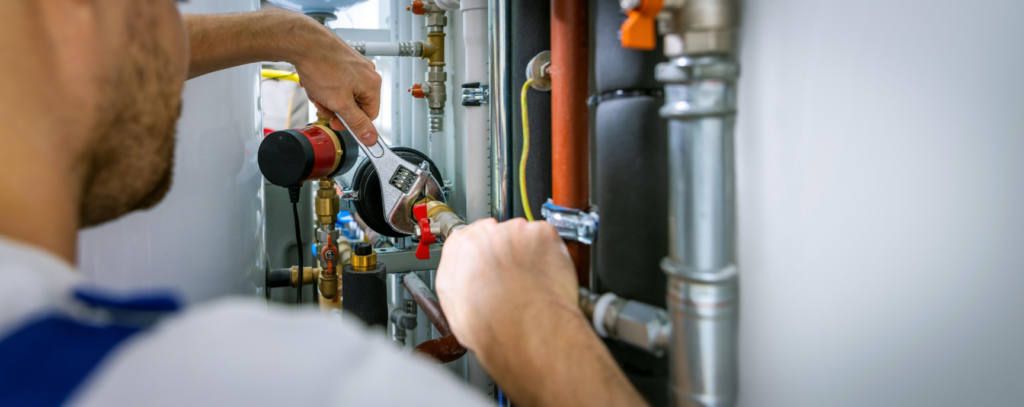 A technician working on a heating system with pipes and valves at Derry Plumbing & Heating in Derry, NH.