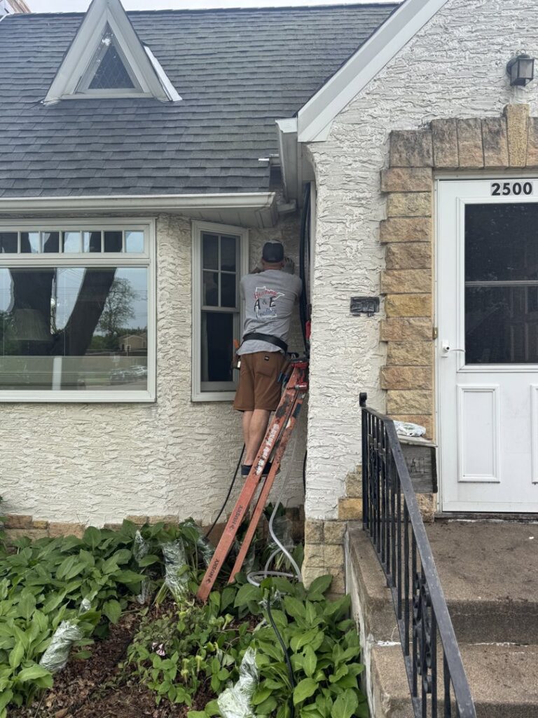 An A&E Heating & Cooling technician working on the exterior of a house from a ladder in Fort Worth, TX.