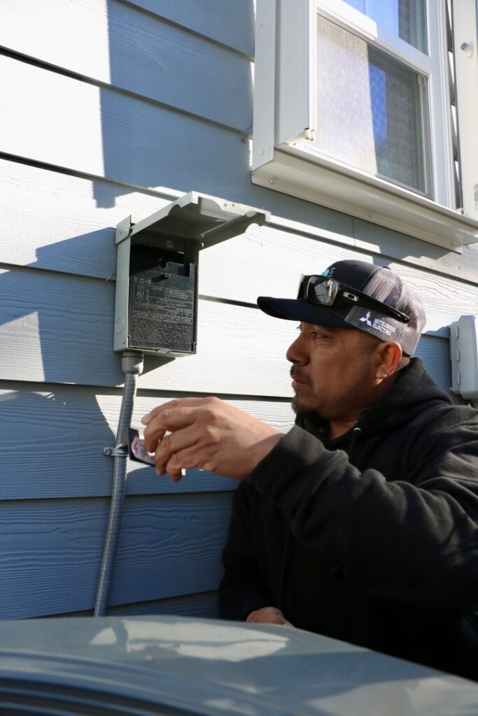 A Green Dot Heating & Air technician working on an HVAC electrical disconnect box outside a home in Wilmington, NC.